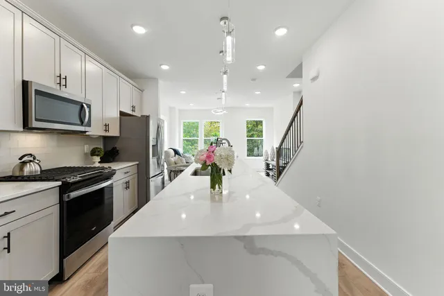 a kitchen with stainless steel appliances kitchen island granite countertop a sink dishwasher a refrigerator and a microwave with wooden floor