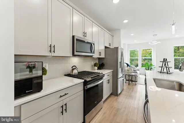 a kitchen with stainless steel appliances granite countertop a stove a sink a refrigerator a microwave a dining table and chairs with wooden floor