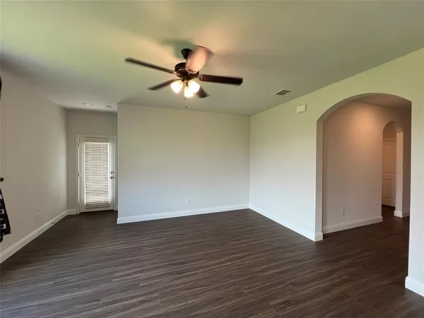 a view of an empty room with wooden floor and a ceiling fan