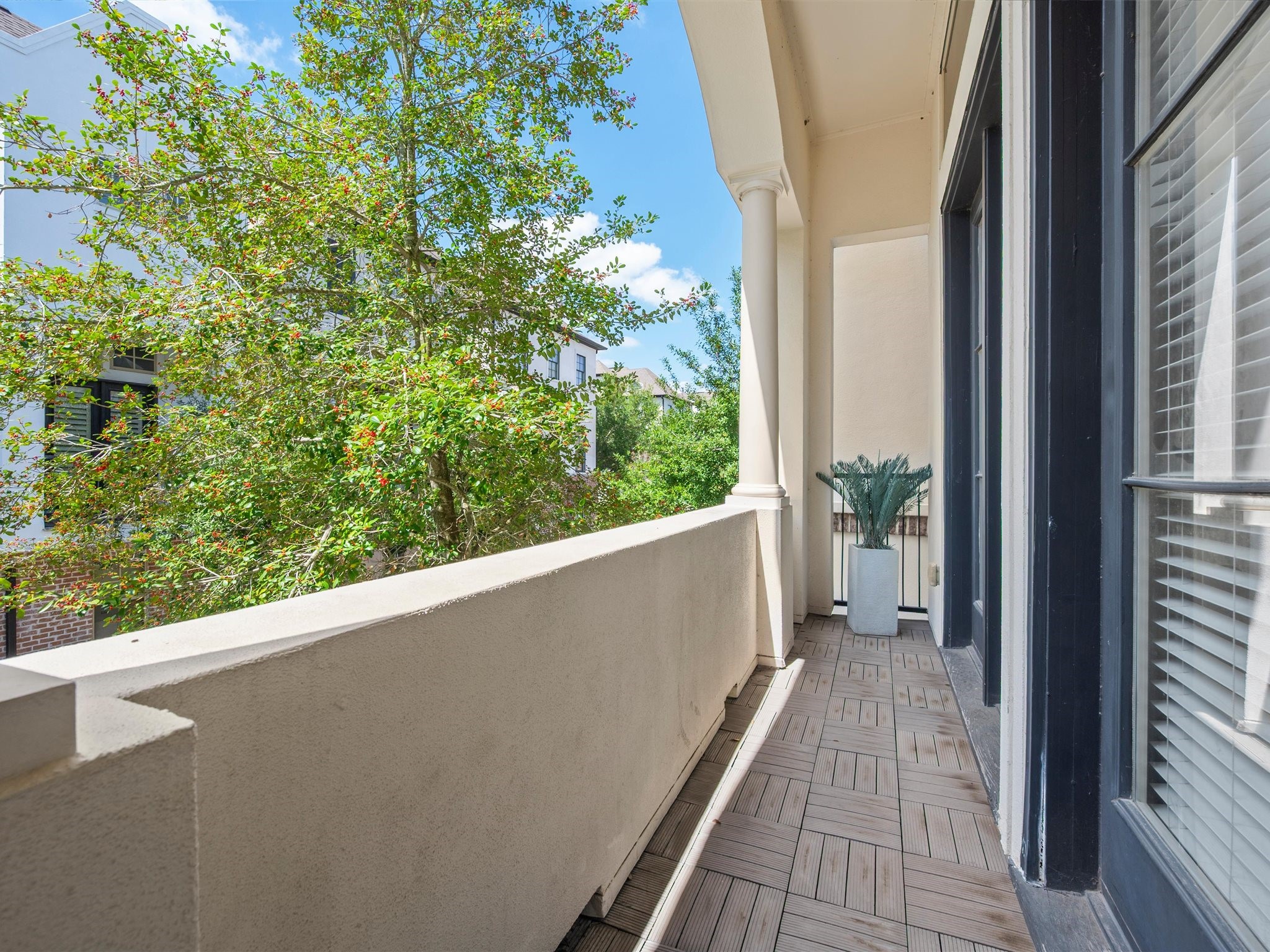 9427 London Bridge Station Houston, TX 77045 - Photo 14 of 30 This photo showcases a charming balcony with elegant columns and wood-patterned flooring. It features a potted plant and offers a tranquil view of lush greenery, perfect for relaxation.