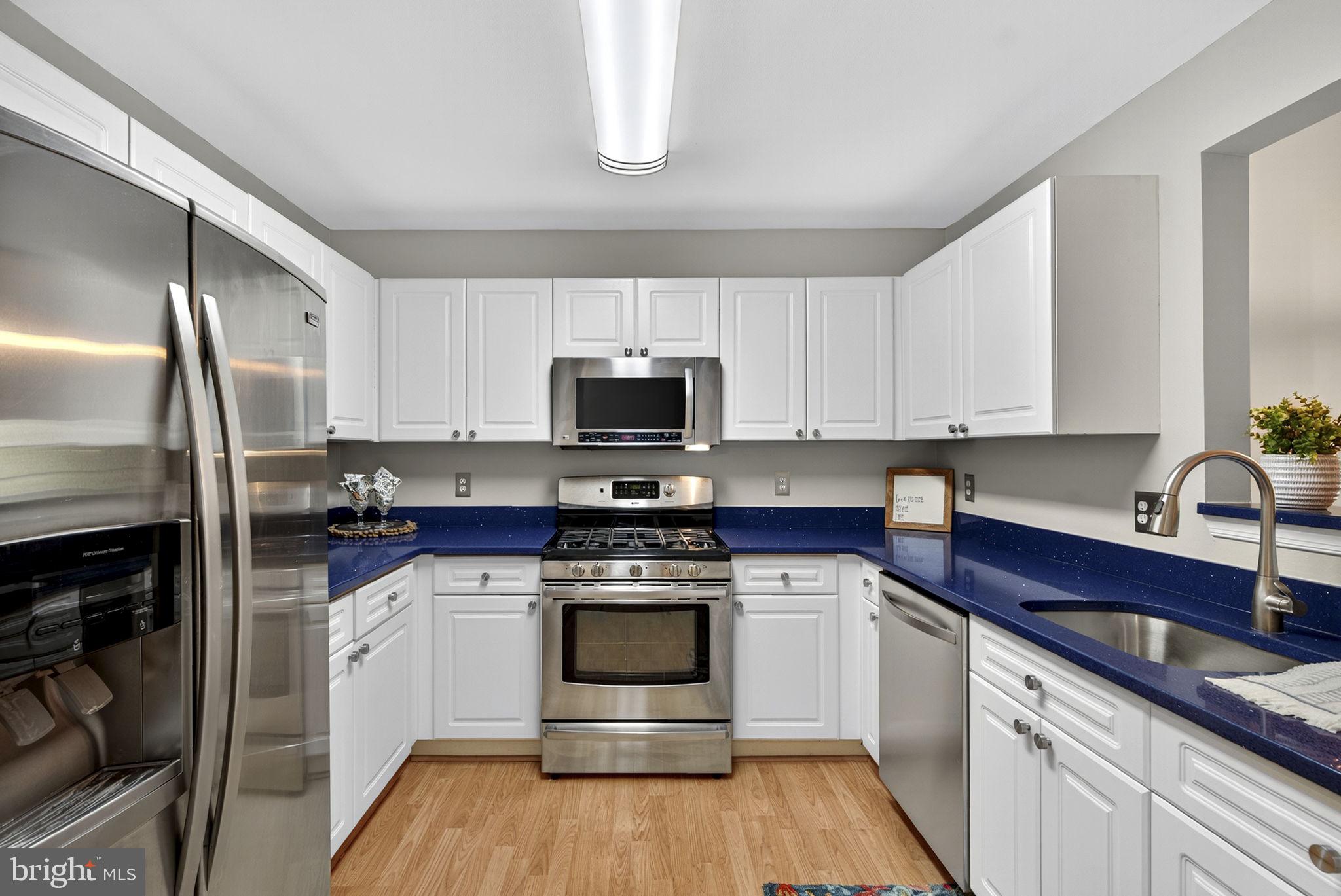 44084 Natalie Terrace, Unit 301 Ashburn, VA 20147 - Photo 33 of 59 a kitchen with stainless steel appliances granite countertop white cabinets a sink a stove a refrigerator and microwave with wooden floor
