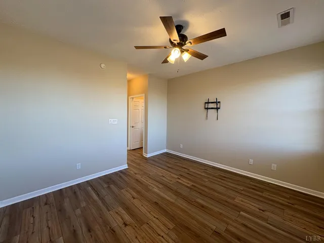 a view of an empty room with wooden floor and a ceiling fan