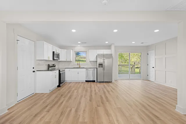 a large white kitchen with a refrigerator a stove top oven a sink dishwasher and white cabinets with wooden floor