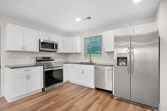 a kitchen with stainless steel appliances granite countertop a refrigerator a stove a sink and white cabinets with wooden floor