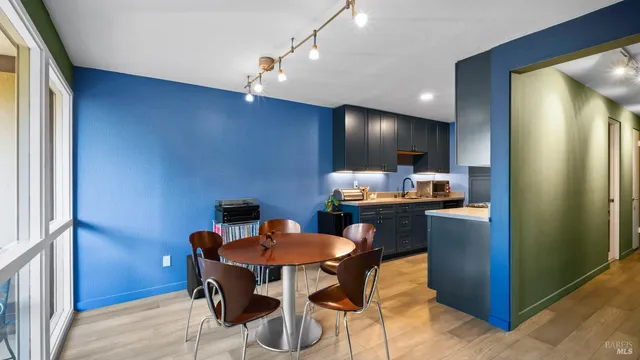 a kitchen with stainless steel appliances kitchen island granite countertop a refrigerator a sink a dining table and chairs with wooden floor