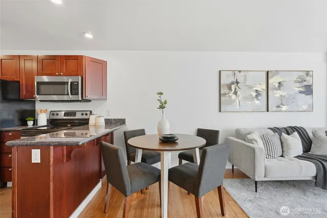 a kitchen with stainless steel appliances granite countertop a stove a sink a microwave a dining table and chairs with wooden floor