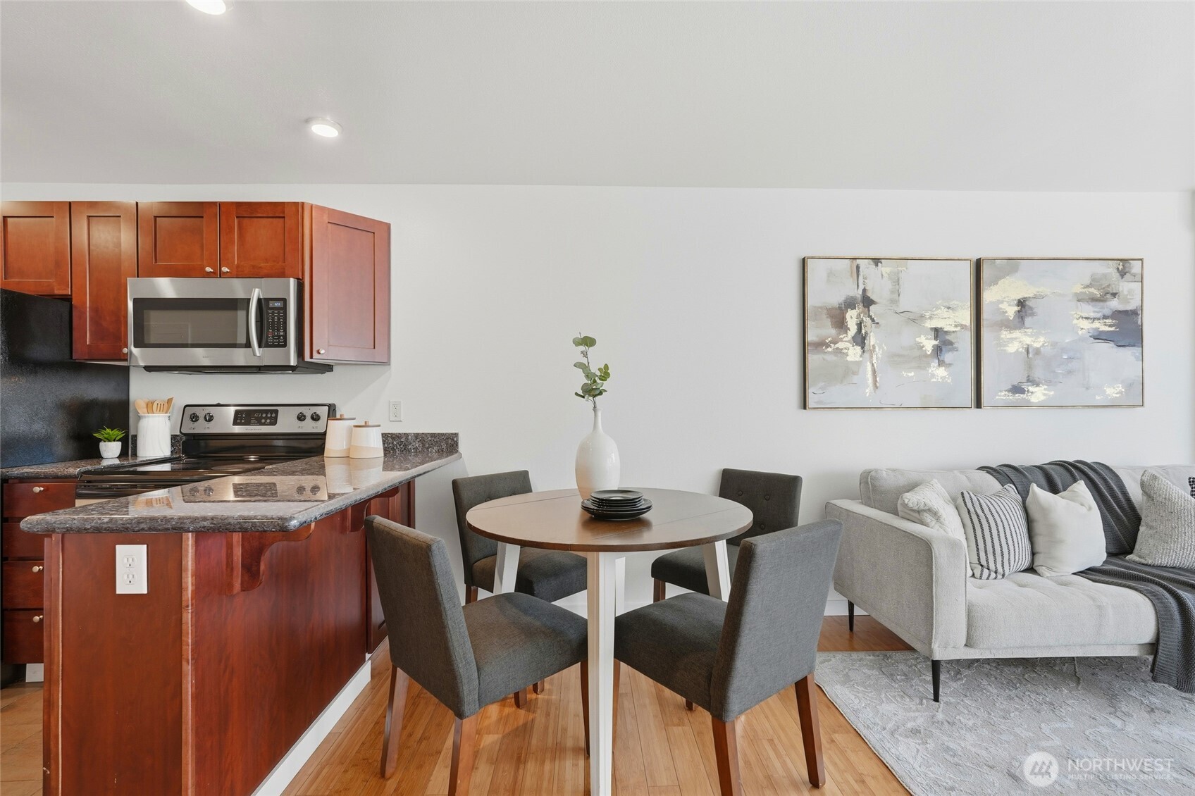 705 East Republican Street, Unit 403 Seattle, WA 98102 - Photo 9 of 28 a kitchen with stainless steel appliances granite countertop a stove a sink a microwave a dining table and chairs with wooden floor
