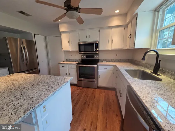 a kitchen with granite countertop stainless steel appliances a sink cabinets and wooden floor