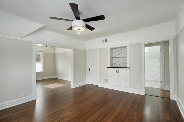a view of an empty room with wooden floor and a ceiling fan