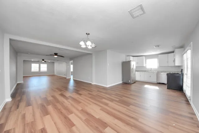 a view of an empty room with wooden floor and kitchen view
