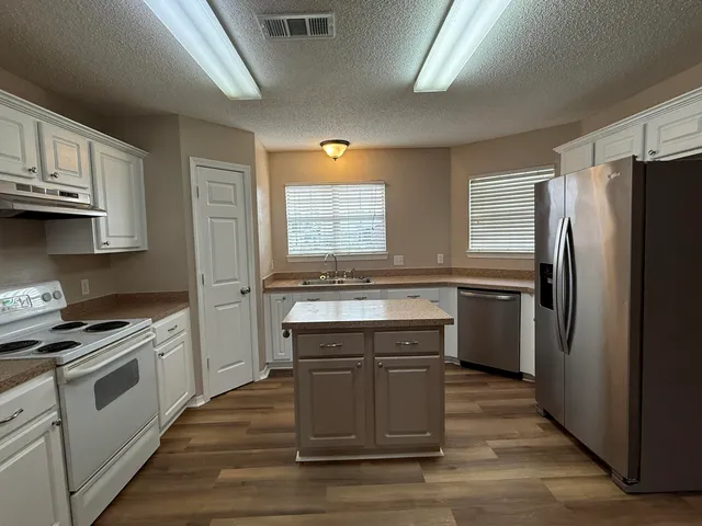 a kitchen with stainless steel appliances granite countertop a stove a sink dishwasher a refrigerator and white cabinets with wooden floor