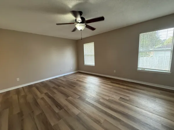 an empty room with wooden floor fan and windows
