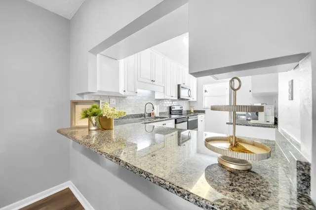a kitchen with granite countertop a sink a stove and white cabinets