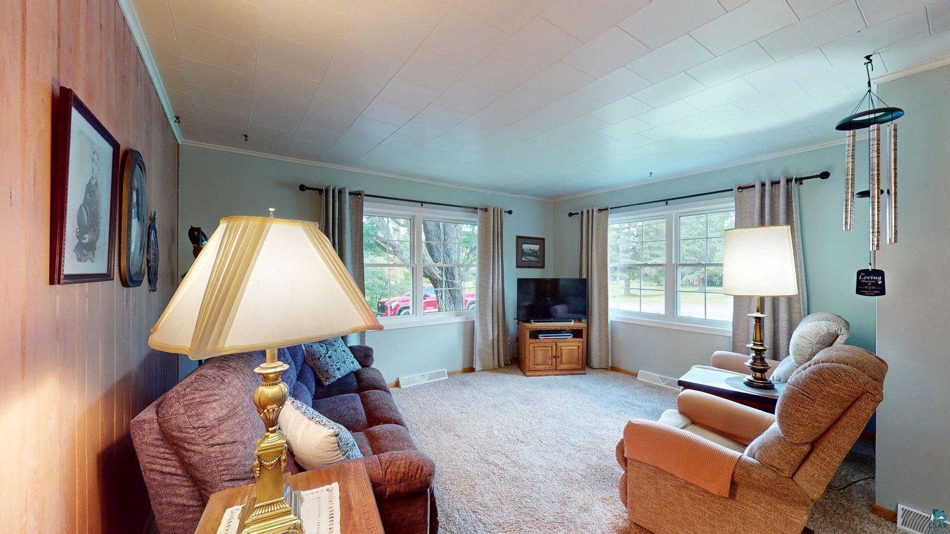 10614 Moose Lake Road Orr, MN 55771 - Photo 16 of 44 Living area featuring two windows, light-colored carpeting, a light blue wall, and wood paneling
