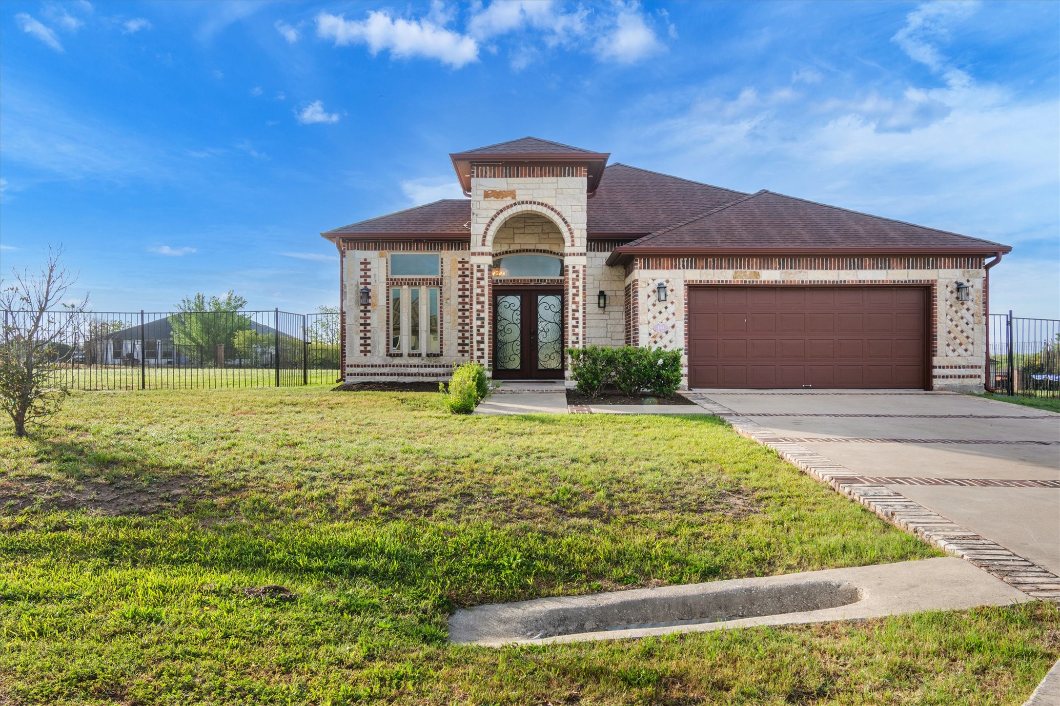 View of front facade featuring french doors, brick siding, driveway, and an attached garage