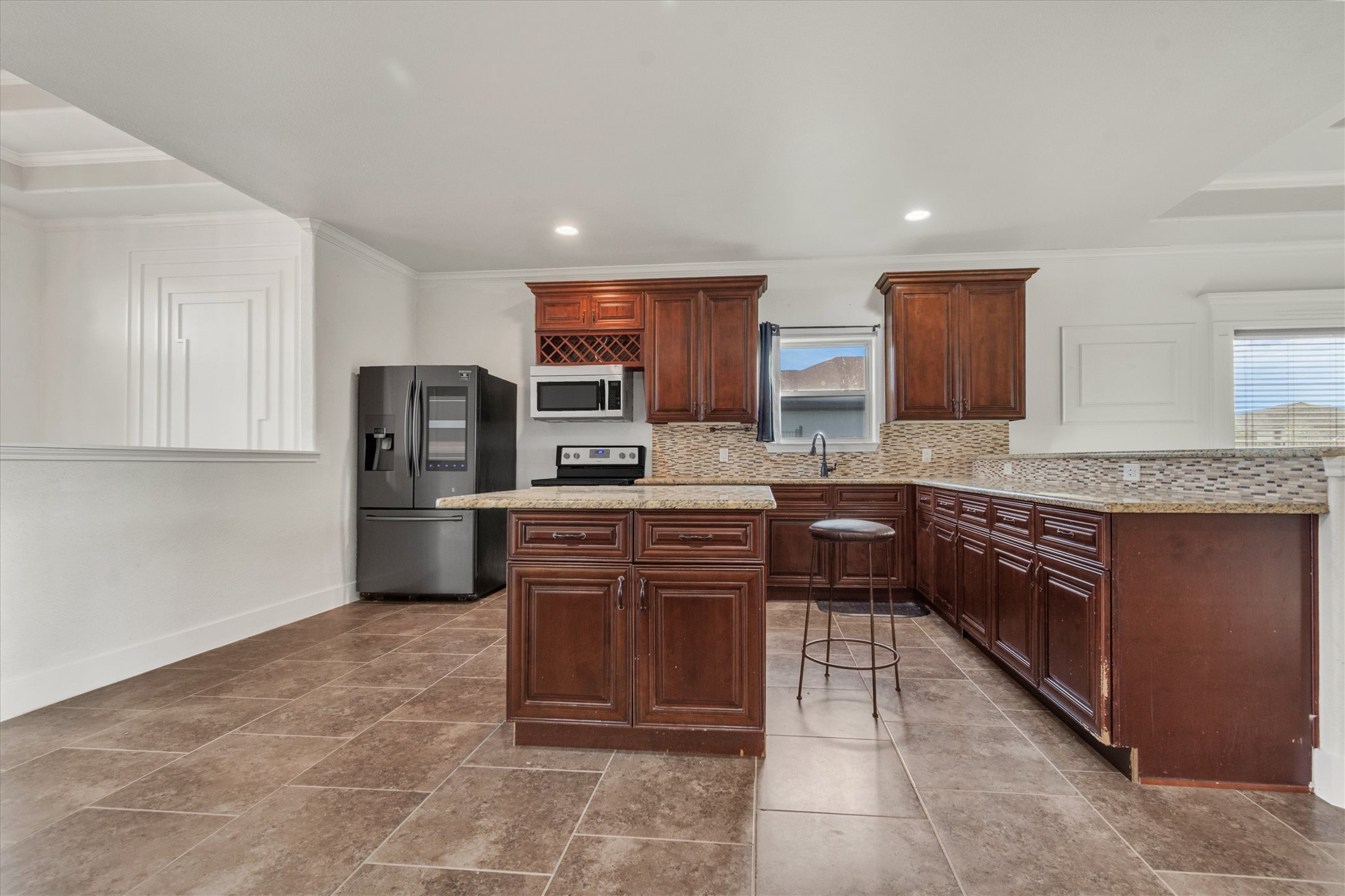 164 Peck Street Kyle, TX 78640 - Photo 6 of 19 Kitchen featuring crown molding, refrigerator with ice dispenser, a peninsula, light stone countertops, and tasteful backsplash