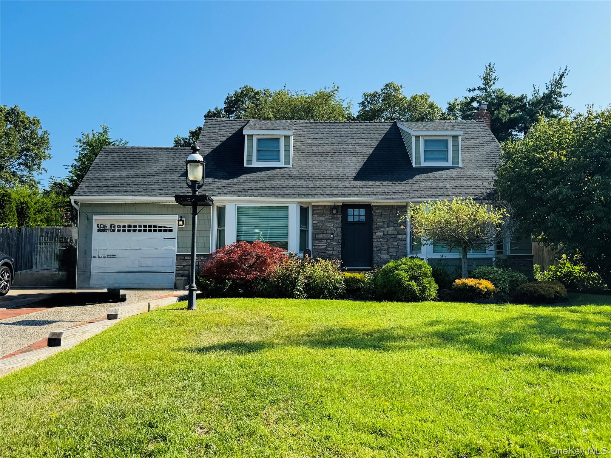Cape cod-style house with stone siding, a garage, a front yard, and roof with shingles