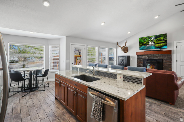1588 West Rim Rock Drive Stockton, UT 84071 - Photo 13 of 61 Open-concept kitchen and living area featuring granite countertops, wood-finish flooring, a stone fireplace with a wood mantle, and vaulted ceilings with recessed lighting