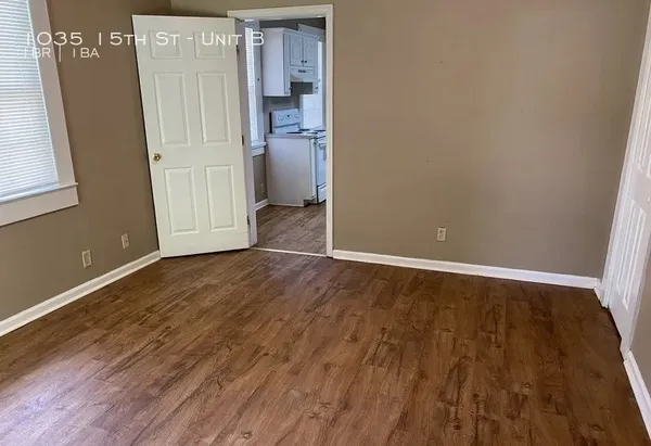 a view of an empty room with wooden floor and a window