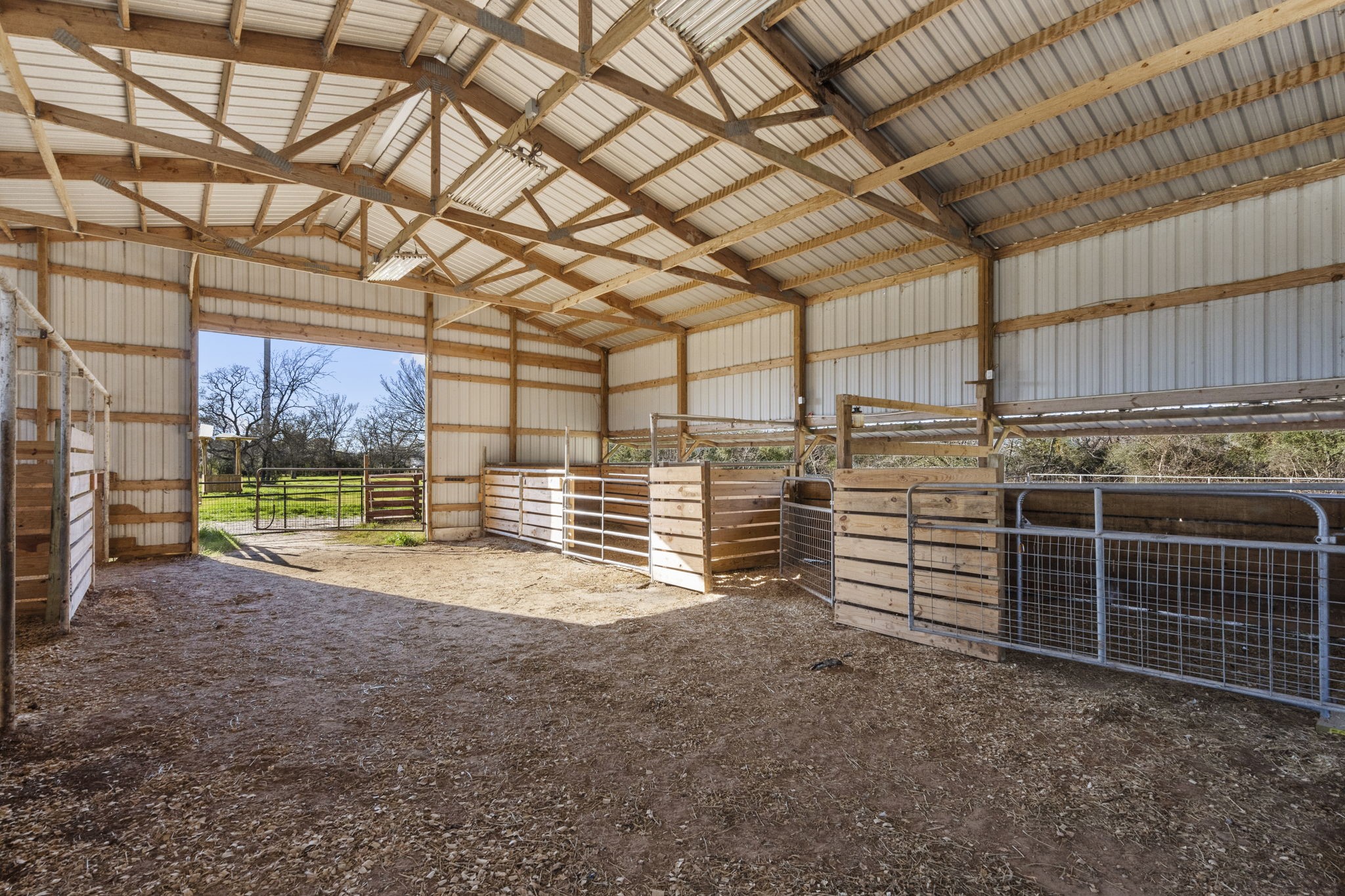 2730 Lawrence Road Kemah, TX 77565 - Photo 43 of 46 This is a spacious barn with a high, sloped roof and multiple horse stalls. It features open sides for ventilation and an entryway leading to a grassy outdoor area. Ideal for equestrian use or livestock housing.