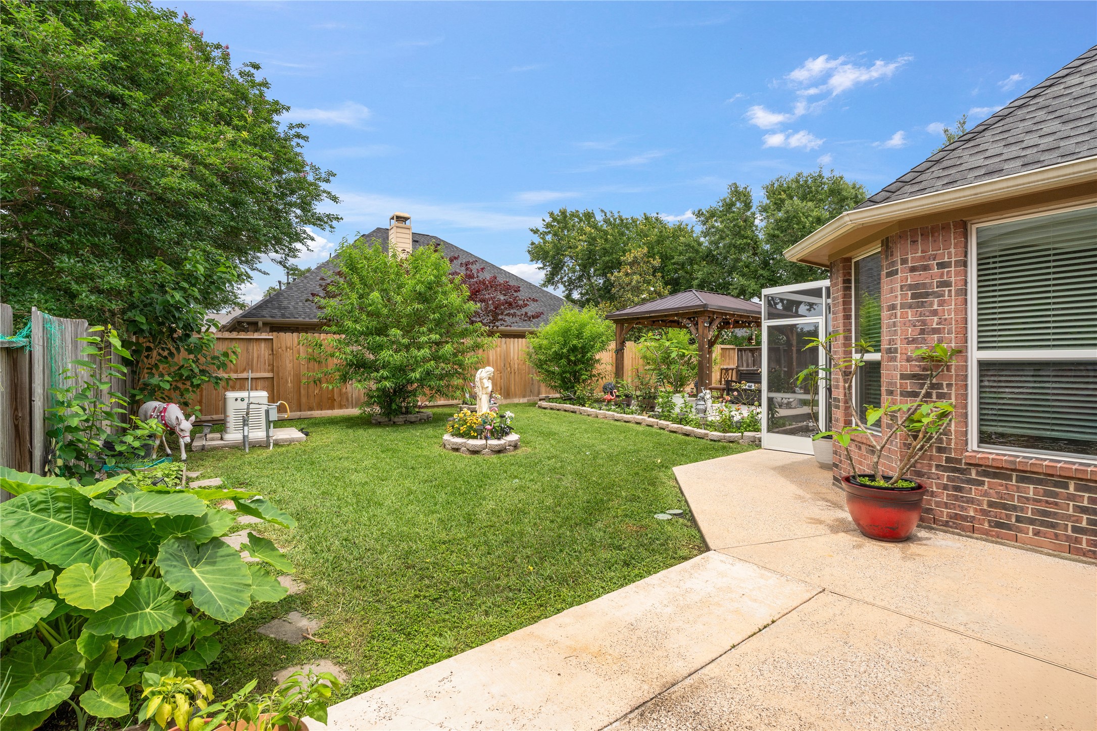 5802 Layton Meadows Lane Spring, TX 77379 - Photo 41 of 42 Side yard/garden view. Lush greenery, mature trees, brick exterior, concrete walkway, and a glimpse of the gazebo in the background. Great establishing shot of the outdoor space.