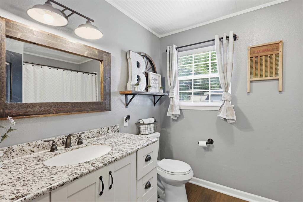 308 West 1st Street Springtown, TX 76082 - Photo 25 of 39 Vanity featuring a solid-surface countertop with an integrated sink, dark bronze-finish faucet, and white shaker-style cabinetry with dark hardware