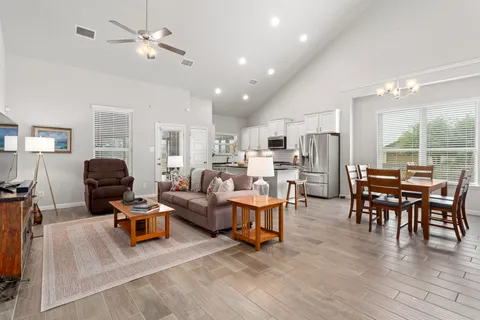 a living room with lots of furniture kitchen view and a wooden floor