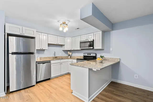 a kitchen with stainless steel appliances granite countertop a refrigerator a stove top oven a sink dishwasher and white cabinets with wooden floor