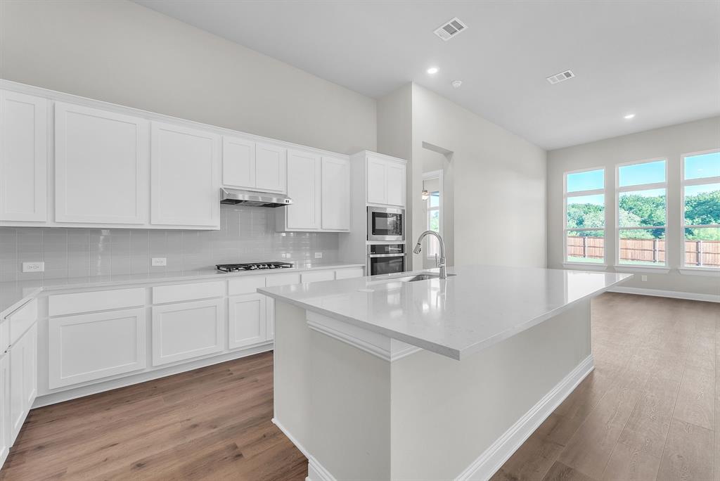1215 Olive Drive Mansfield, TX 76063 - Photo 11 of 28 a kitchen with stainless steel appliances granite countertop a sink a stove a refrigerator and white cabinets with wooden floor
