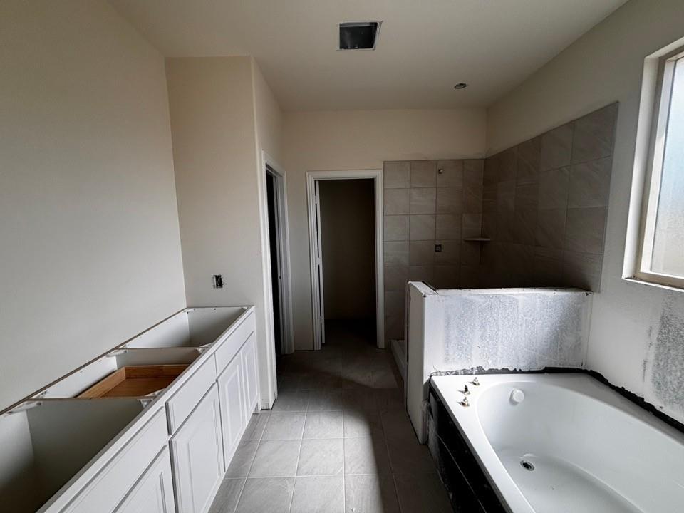 Built-in bathtub with tiled surround, large window, full-height wall tiling, and pre-installed vanity cabinetry