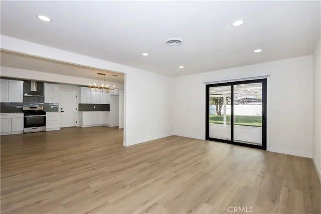a view of empty room with wooden floor and kitchen