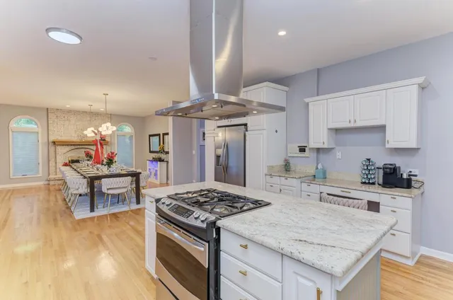 a kitchen with stainless steel appliances granite countertop a stove top oven a refrigerator a sink and white cabinets with wooden floor