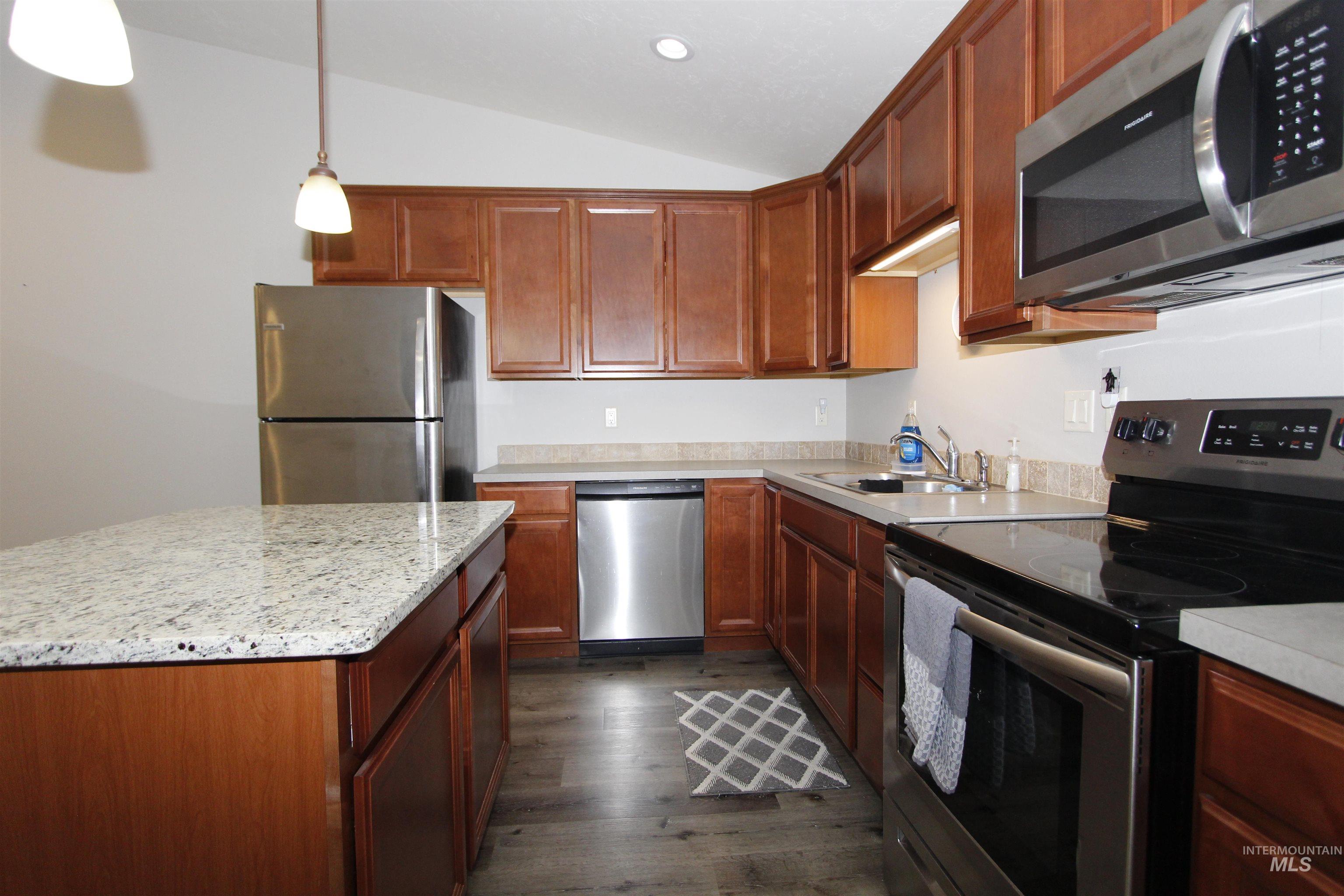 3434 5th Street, Unit B Lewiston, ID 83501 - Photo 3 of 14 Kitchen featuring appliances with stainless steel finishes, vaulted ceiling, dark wood-style floors, hanging light fixtures, and a center island