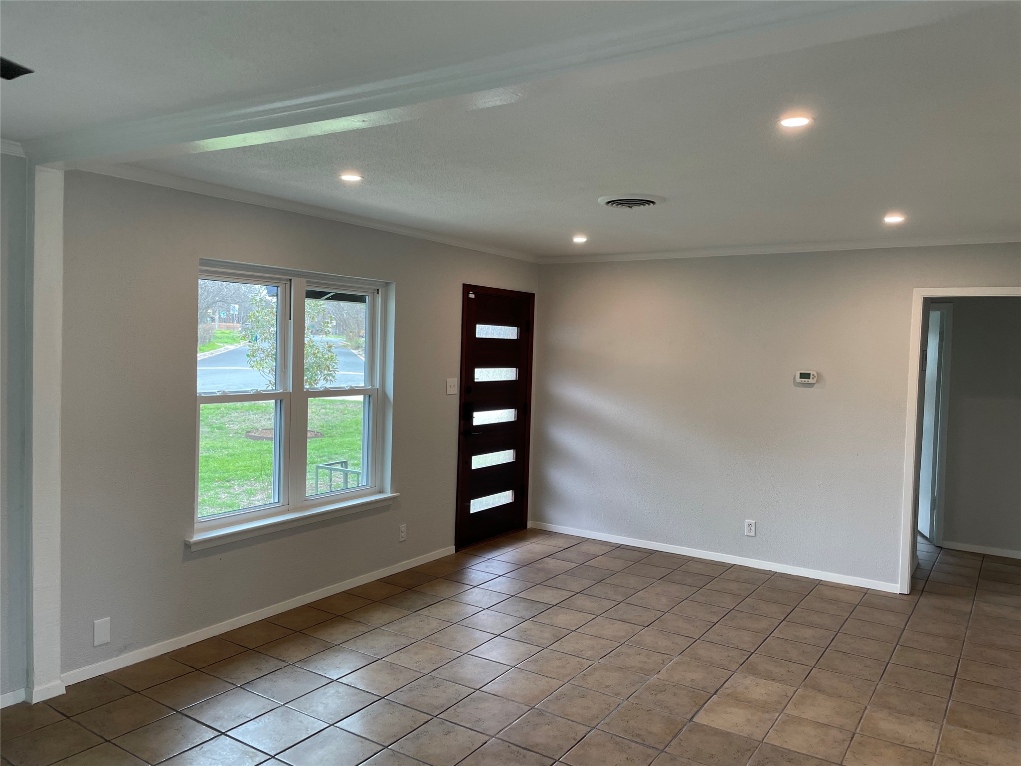 4619 Jinx Avenue, Unit A Austin, TX 78745 - Photo 1 of 21 Spacious room featuring tile flooring, a dark wood-finish entry door with frosted glass panels, a double-paned window, recessed ceiling lighting, and crown molding