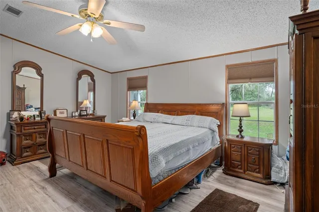 a bedroom with a bed a dresser and potted plants on the wooden floor