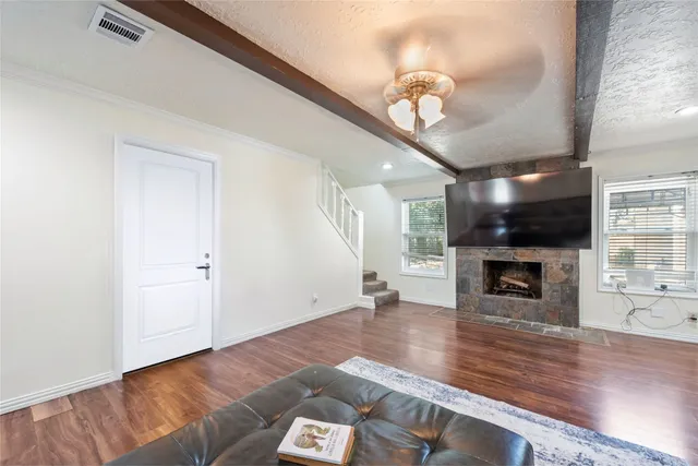 a view of a livingroom with wooden floor a fireplace a ceiling fan and windows