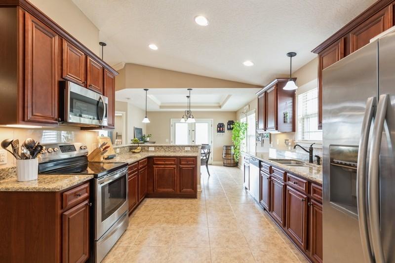 2693 Hartman Court Navarre, FL 32566 - Photo 11 of 34 a large kitchen with stainless steel appliances granite countertop a stove top oven a sink dishwasher a refrigerator and a dining table with wooden cabinets