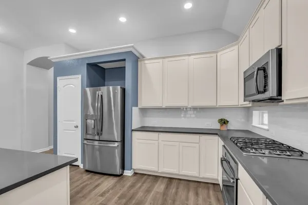 a kitchen with stainless steel appliances granite countertop a refrigerator a sink a stove and white cabinets with wooden floor