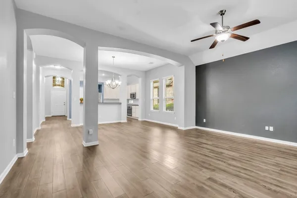 a view of an empty room with wooden floor and a ceiling fan