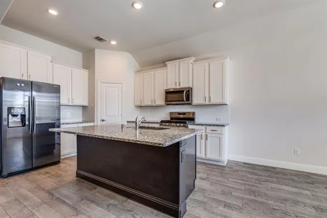 a kitchen with stainless steel appliances granite countertop a stove top oven a sink and dishwasher a refrigerator with wooden floors