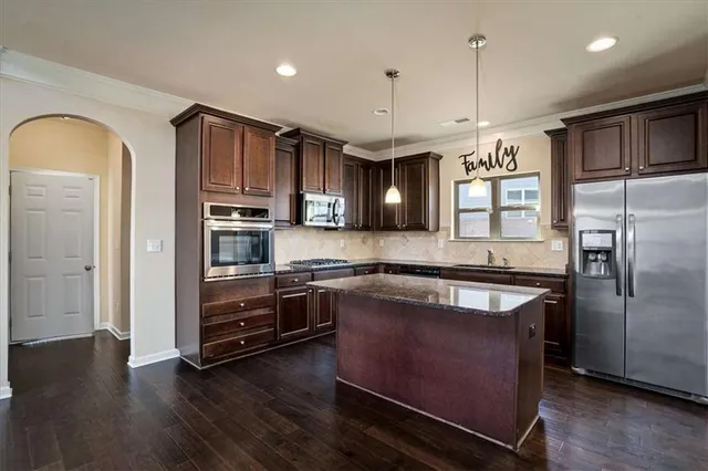 a kitchen with stainless steel appliances granite countertop a refrigerator a stove and a wooden floors