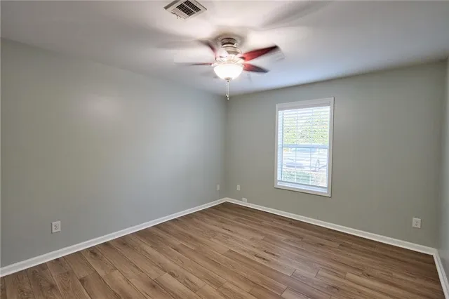 an empty room with wooden floor fan and windows
