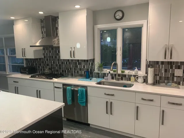 a kitchen with a sink dishwasher a stove and white cabinets with wooden floor