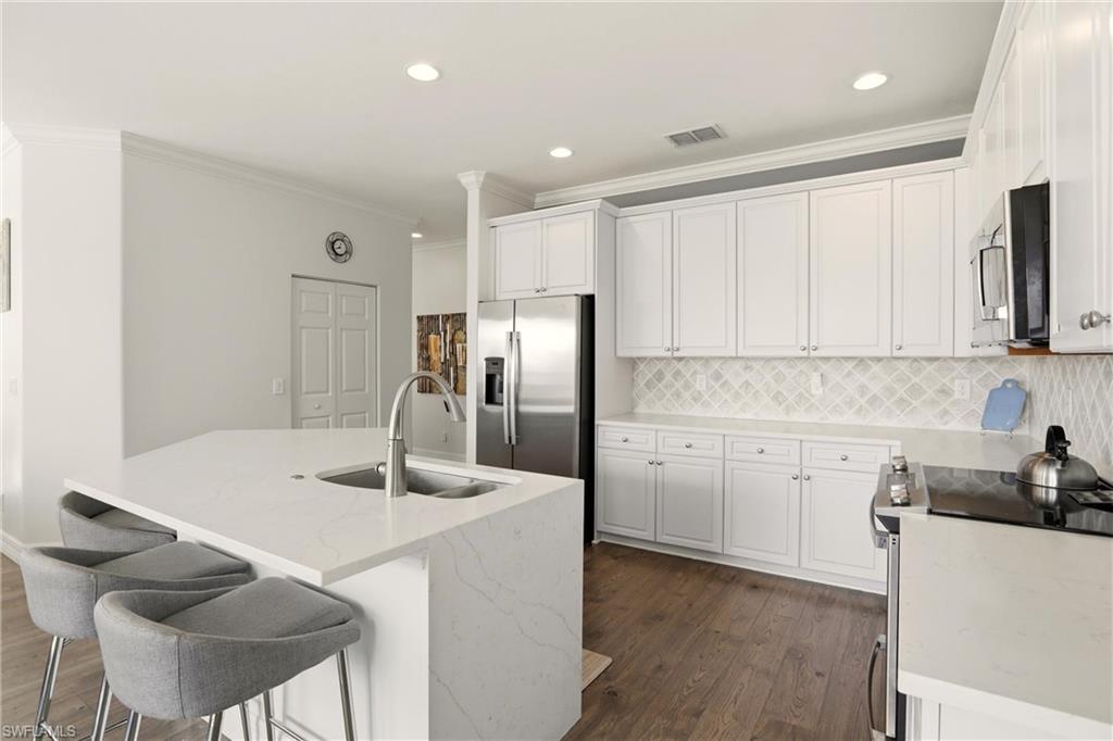2150 Khasia Point Naples, FL 34119 - Photo 9 of 39 Kitchen featuring appliances with stainless steel finishes, white cabinetry, light stone counters, crown molding, and a center island with sink