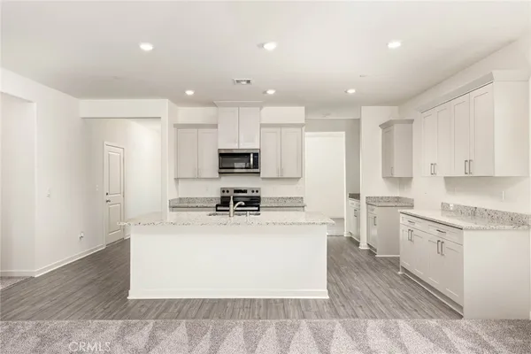 a large kitchen with stainless steel appliances kitchen island granite countertop a stove a sink a refrigerator and white cabinets with wooden floor