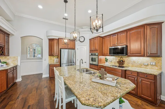 a large kitchen with granite countertop a stove a sink a center island and wooden floor