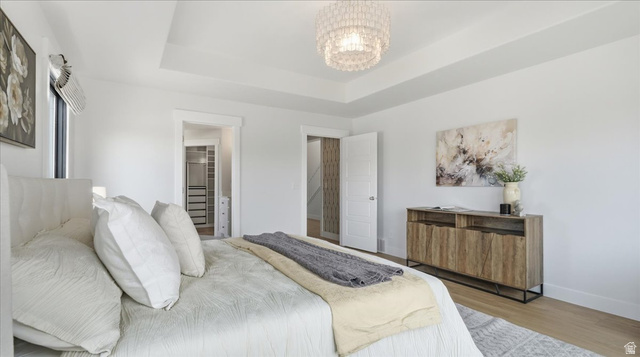 2038 East Ranch Road Eagle Mountain, UT 84005 - Photo 19 of 66 Spacious bedroom featuring a tray ceiling with a chandelier, wood-finish flooring, and bright white walls