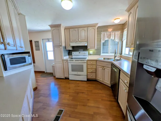 a kitchen with stainless steel appliances a stove a refrigerator a sink a dining table and chairs with wooden floor