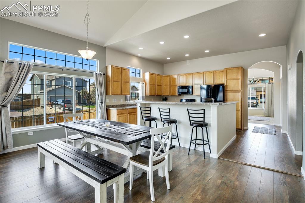 6446 Dancing Moon Way Colorado Springs, CO 80911 - Photo 9 of 42 a kitchen with stainless steel appliances kitchen island granite countertop a stove a refrigerator a sink a dining table and chairs with wooden floor