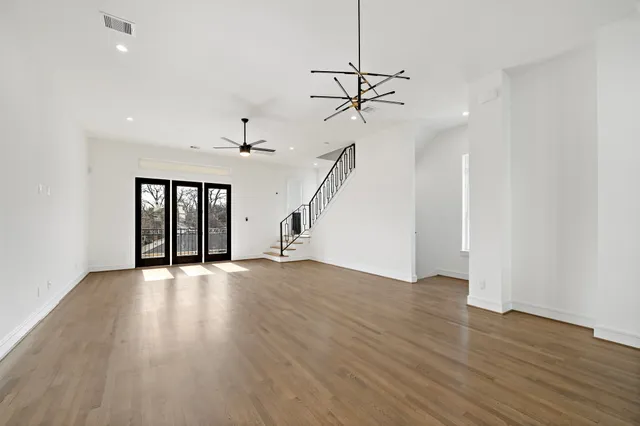 a view of an empty room with wooden floor ceiling fan